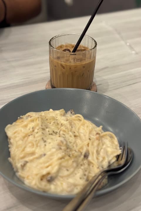 Spaghetti alfredo dengan saus krim dalam mangkuk keramik, ditemani es kopi
