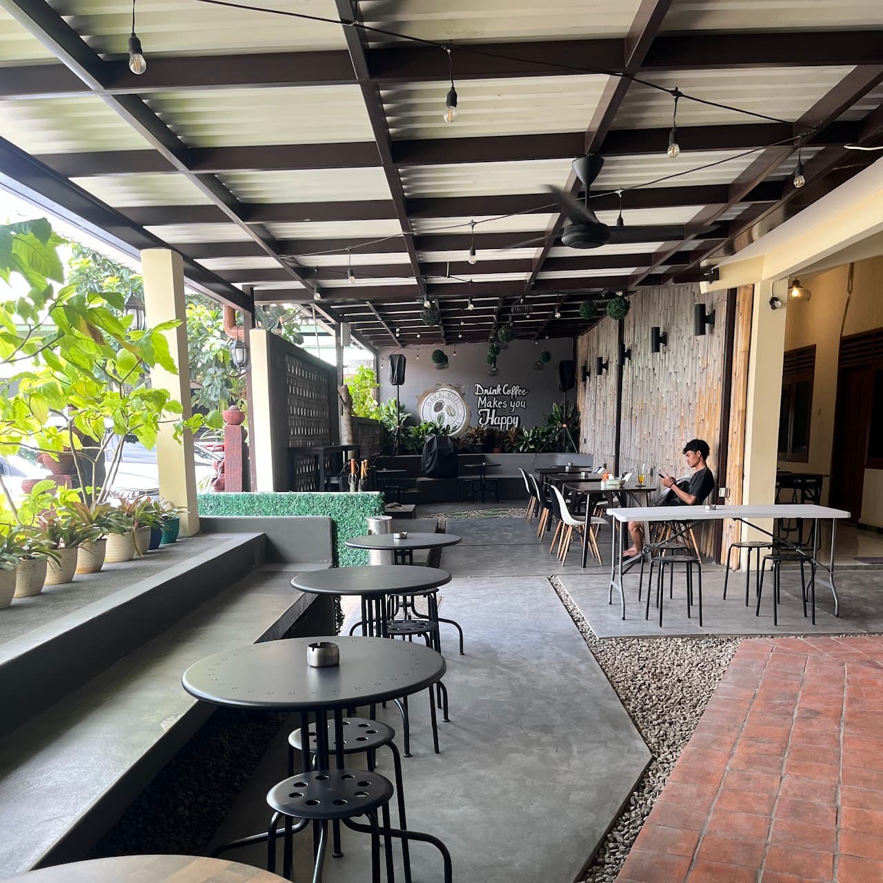 Teras terbuka BAKALKOPI dengan meja bundar, tanaman, dan dinding mural