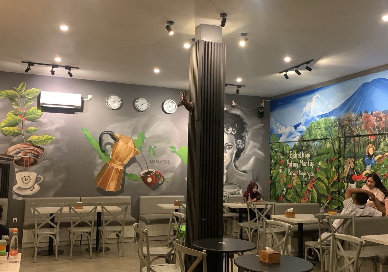 Ruang dalam BAKALKOPI dengan mural proses kopi dan meja kayu